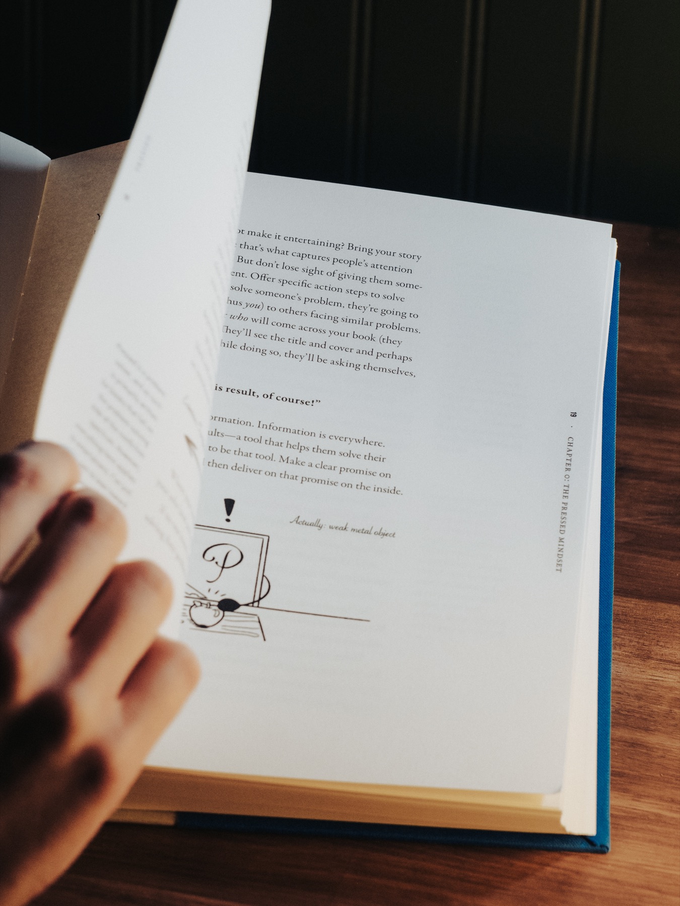 A hand turning a page with a small illustration