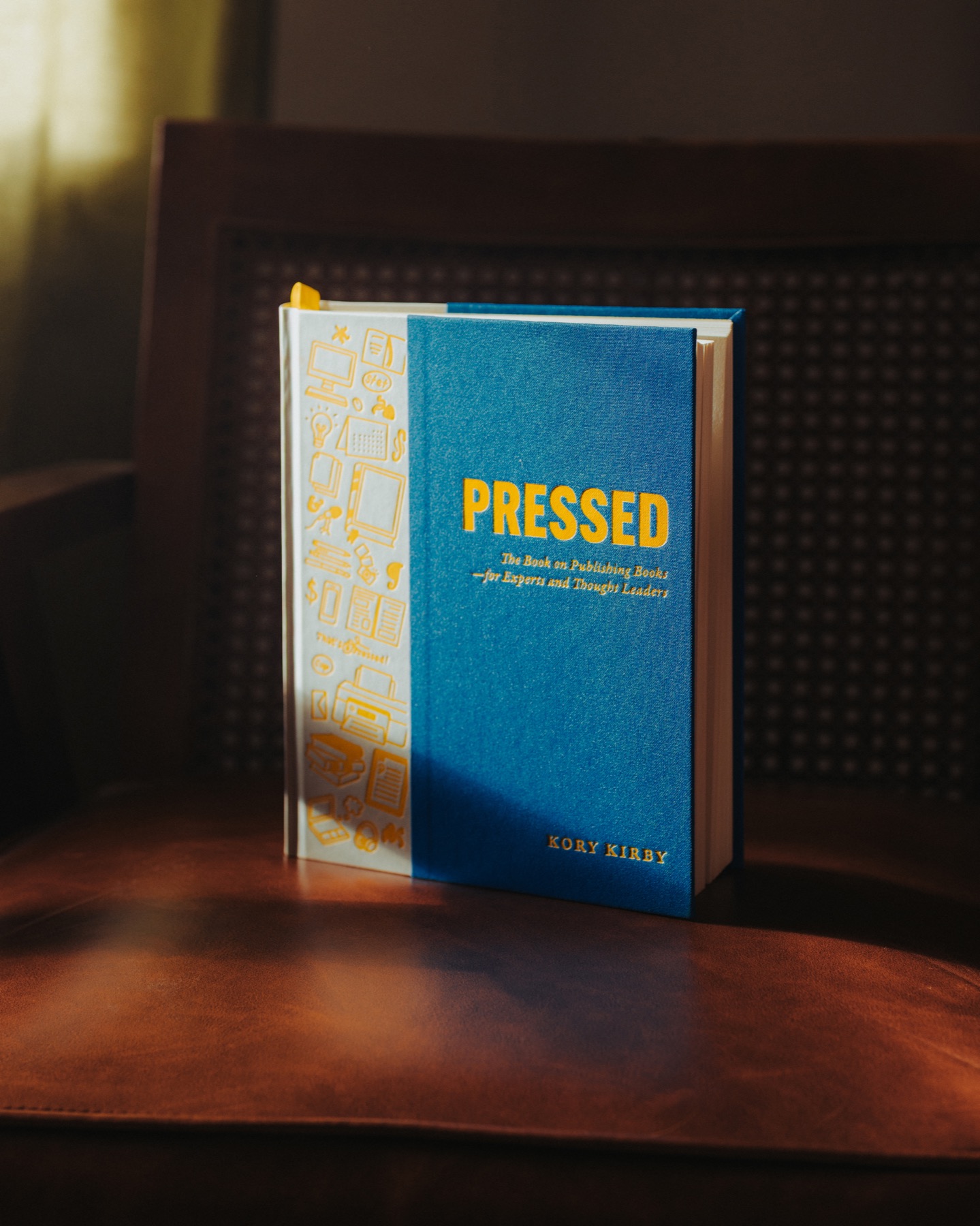 The Pressed hardcover standing on a wooden chair in warm window light